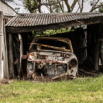 A rusty old car awaiting removal in a shed, near a local junk removal service.